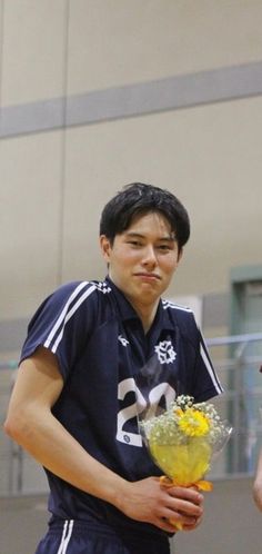 a young man holding a bouquet of flowers in his hand while standing on a basketball court