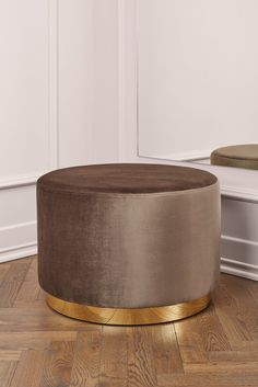 a round ottoman sitting on top of a hard wood floor next to a white wall