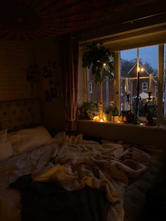 an unmade bed sitting in front of a window with candles on the windowsill