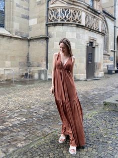 a woman in a brown dress is standing on a cobblestone street near an old building