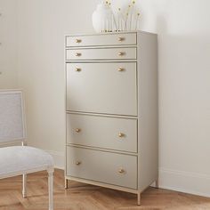 a white chair sitting in front of a tall chest of drawers on top of a hard wood floor