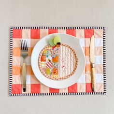 a white plate topped with an apple next to a fork and knife on top of a checkered place mat