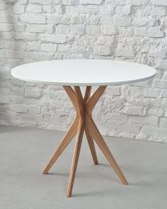 a white round table with wooden legs in front of a brick wall and grey concrete floor