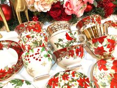 a table topped with plates and cups covered in red flowers on top of a white table cloth