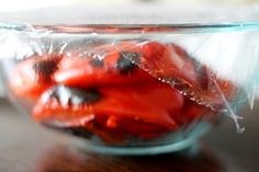 a glass bowl filled with sliced strawberries on top of a wooden table next to a plastic bag