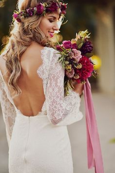 the back of a bride's dress with flowers in her hair and a pink ribbon around her neck