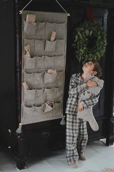 a young boy holding a stuffed animal in front of a wall hanging on a coat rack