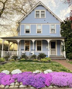 a blue house with purple flowers in the front yard