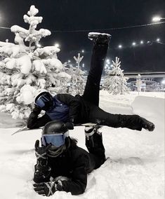 a snowboarder laying on the ground in front of a snowy tree at night