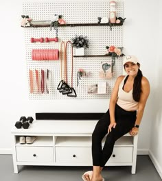 a woman sitting on top of a white bench in front of a wall mounted jewelry rack