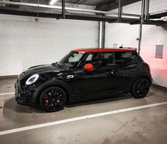 a small black and red car parked in a parking garage next to a white wall