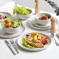 a white table topped with plates and bowls filled with different types of food next to utensils