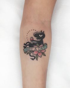 a black cat tattoo on the arm with a ribbon around it's neck that says, not a cat