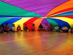 a group of children sitting in front of colorful umbrellas on the floor at a school