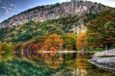 a lake surrounded by trees in front of a large rock face with fall foliage on it