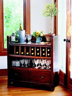 a wooden cabinet filled with wine glasses next to a window and potted plant on top of it