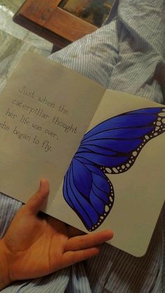 a hand holding an open book with a blue butterfly on the cover and a poem written in it