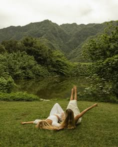 a woman laying on the grass in front of a lake