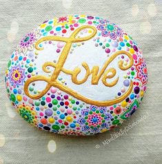 a painted rock with the word love in gold on it's center and surrounded by multicolored dots