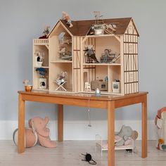 a wooden doll house sitting on top of a table next to stuffed animals and toys