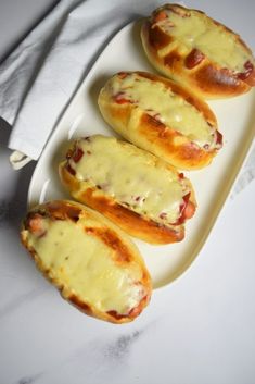 three hot dogs covered in cheese sit on a white platter next to a napkin