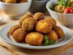 some fried food is on a white plate near bowls of salad and watermelon