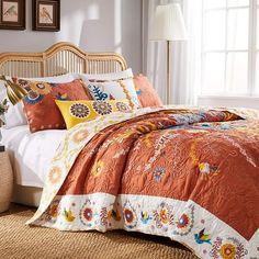 a bed with an orange and yellow quilt on it