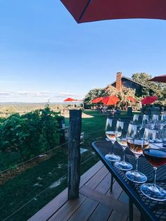 several glasses of wine are sitting on a table with red umbrellas over the tables