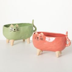 two ceramic cat planters sitting next to each other on a white surface with one green and the other pink