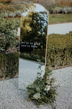 a mirror sitting on top of a sidewalk next to bushes