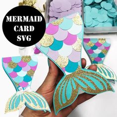 the mermaid card svg is being held up by someone's hand with gold and blue