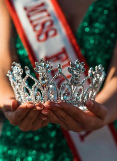 a close up of a person holding a tiara in front of her face and wearing green sequins