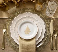 a place setting with gold and white plates, silverware and napkins on a wooden table