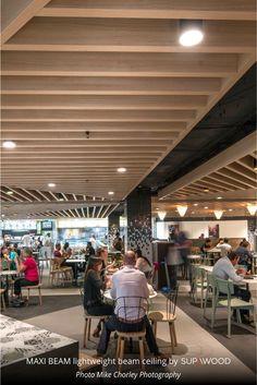 people sitting at tables in a restaurant with wood beams on the ceiling and overhead lighting