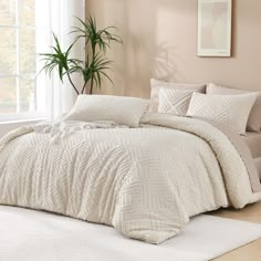 a white bed in a bedroom next to a window with a potted plant on the side