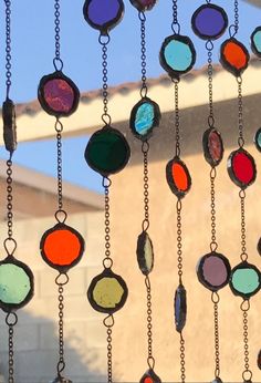 several different colored stained glass pieces hanging from chains in front of a building with a sky background