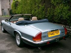 a silver convertible car parked in front of a hedged area with a black top