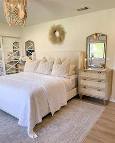 a white bed sitting in a bedroom next to a dresser with a mirror on top of it