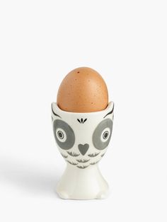 an egg in a ceramic cup with eyes and nose painted on the side, against a white background