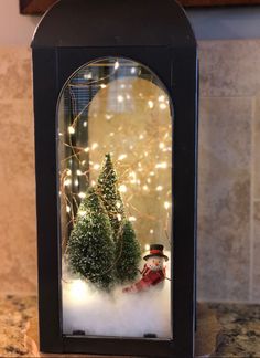 a snow globe with christmas trees and a snowman in the middle on a kitchen counter