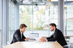 two men sitting at a table in an office