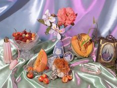 a table topped with fruit and flowers on top of a blue satin covered table cloth