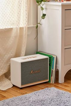 a white radio sitting on top of a wooden floor next to a dresser and window