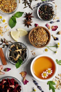 several bowls filled with different types of teas and herbs on a white tablecloth