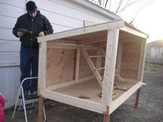 a man standing next to a wooden structure in front of a house with the door open