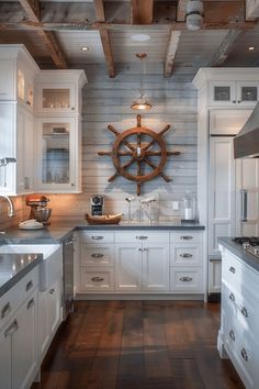 a kitchen with white cabinets and wood flooring has a ship wheel on the wall