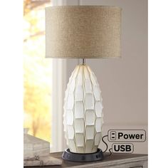 a table lamp that is on top of a wooden dresser next to a window with the power usb plugged in