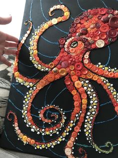 an octopus made out of buttons on a piece of black fabric with white and orange swirls