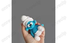 a hand holding a small blue stuffed animal with a white hat on it's head