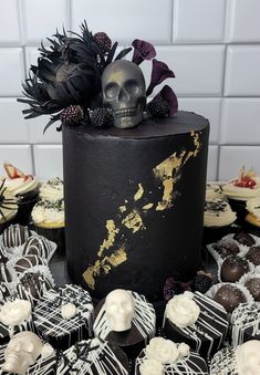 there is a black cake with white frosting and skulls on the top, surrounded by other cupcakes